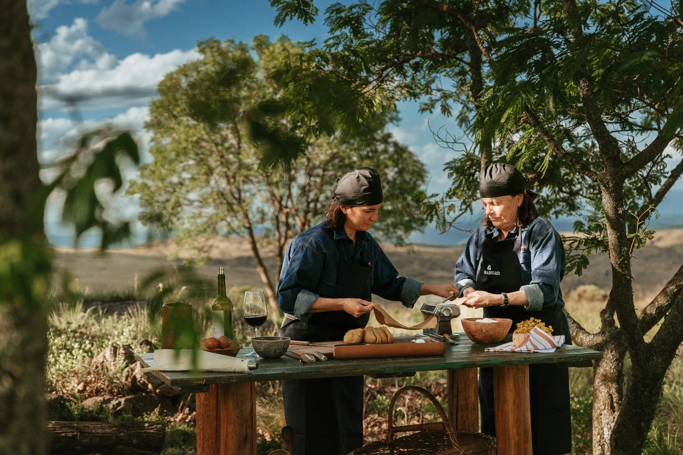Luciana and Ani making pasta outdoors, the hills behind