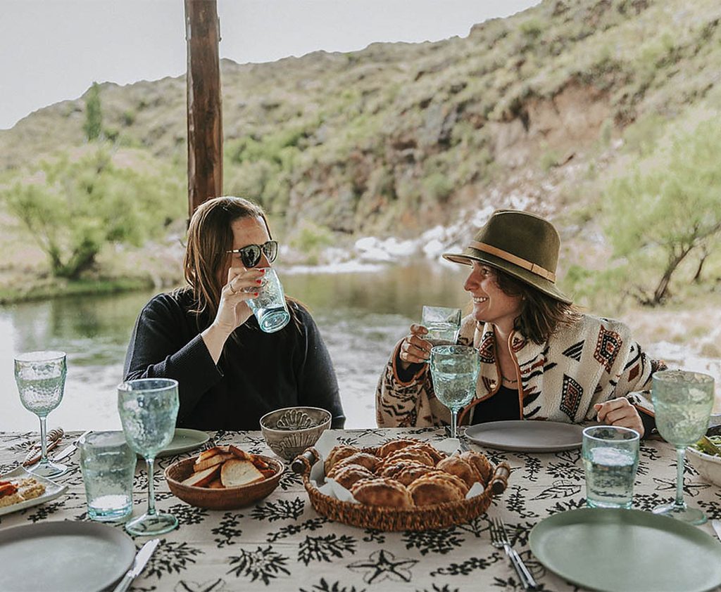 Lunch at the long table by the river — empanadas, glasses, conversation