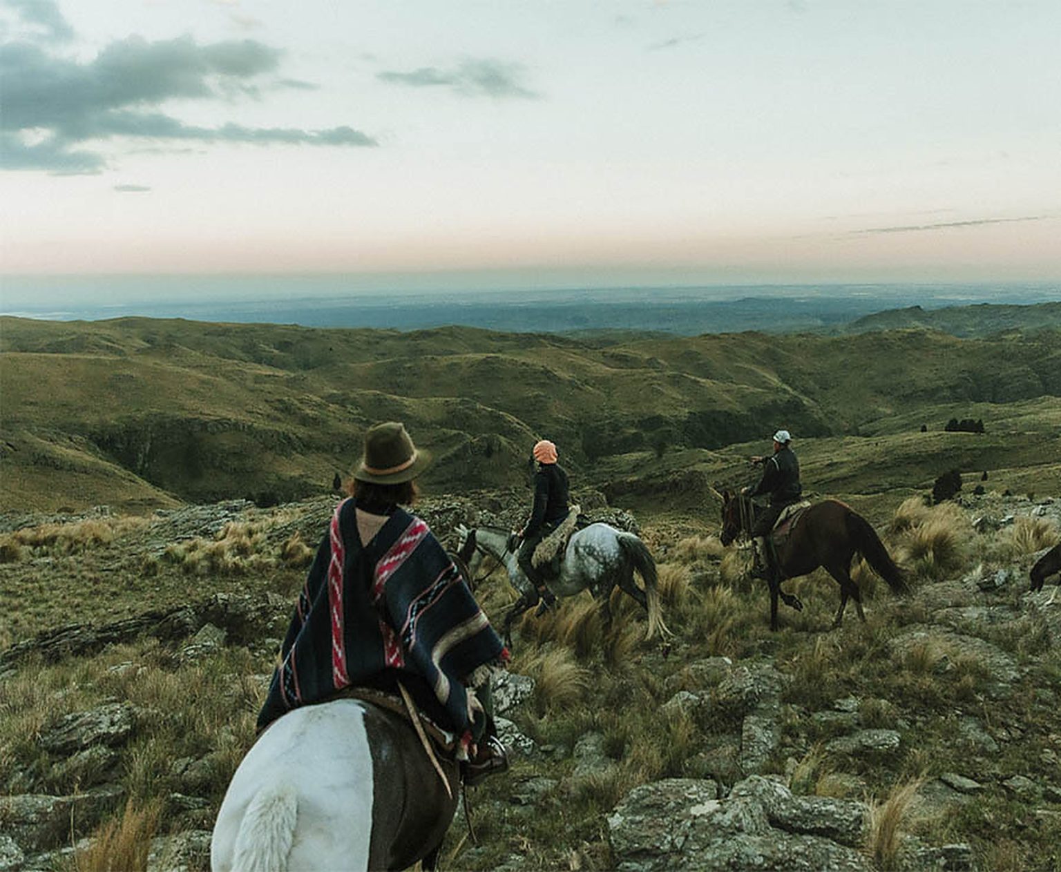 Three riders heading into the hills at dusk, the Sierras de Córdoba stretching out below